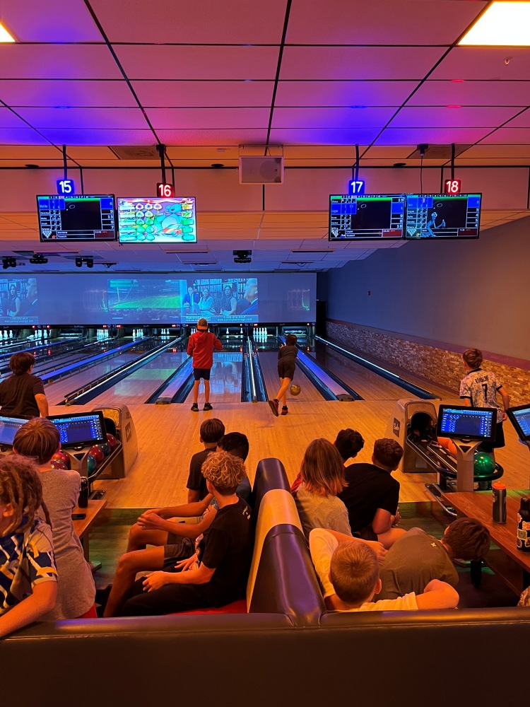 Summer campers fill the seating area of a bowling alley, watching friends roll balls down the lanes during a South Cape Community Center camp bowling day.